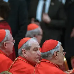 Księża w czerwonych szatach i biretach, którzy mogą zostać kardynałem, siedzą w rzędzie.