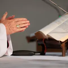 Dłonie biskupa złożone do modlitwy przed księgą. Kto nie może być świadkiem bierzmowania? Tylko ten, kto nie wierzy.