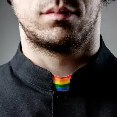 Broda i usta mężczyzny w czarnej koszuli. Widoczny tęczowy kołnierzyk, symbolizujący, co to jest pastor otwarty na wszystkich.