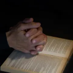 Dłonie złożone w modlitwie nad otwartą księgą. Czy spowiedź jest obowiązkowa? Pytanie w ciszy.