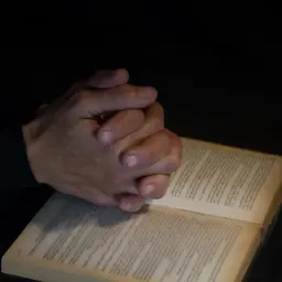Dłonie złożone w modlitwie nad otwartą księgą. Czy spowiedź jest obowiązkowa? Pytanie w ciszy.