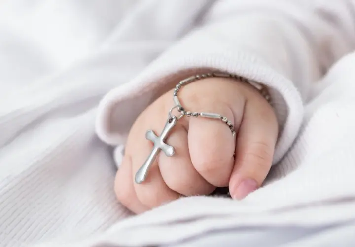 Dziecięca dłoń z krzyżykiem na nadgarstku. Zastanawiasz się, ile trwa msza z chrztem?