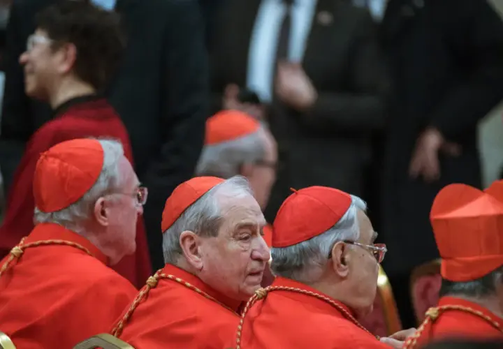 Księża w czerwonych szatach i biretach, którzy mogą zostać kardynałem, siedzą w rzędzie.