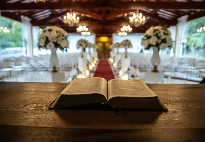 Otwarta Biblia na drewnianym stole. W tle udekorowana sala z krzesłami i czerwonym dywanem. Zastanawiasz się, ile trwa msza święta w tygodniu?