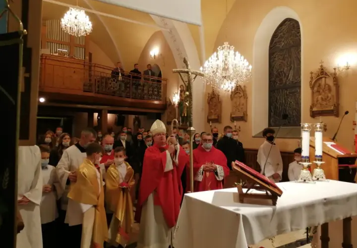 Biskup w czerwonej szacie, który jest szafarzem bierzmowania, błogosławi wiernych w kościele.