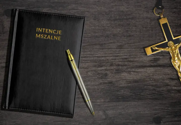 Czarny notatnik z napisem "INTENCJE MSZALNE", długopis i złoty krzyż. Zastanawiasz się, ile kosztuje msza gregoriańska w Niepokalanowie?
