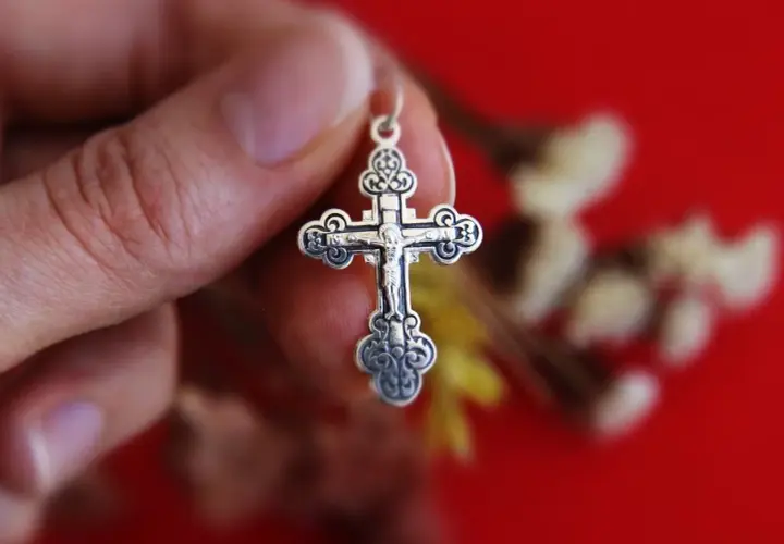Srebrny krzyż prawosławny w dłoni. Różnice między prawosławiem a katolicyzmem mogą być widoczne w symbolice.