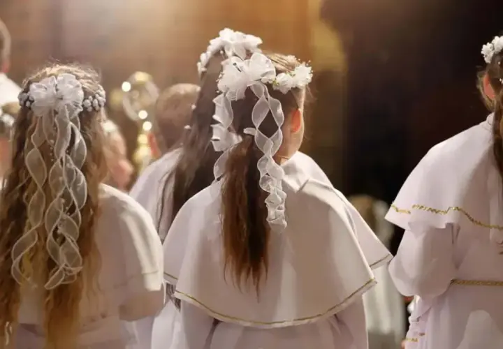 Dzieci w białych strojach, z wiankami na głowach, czekają na moment, kiedy jest komunia.