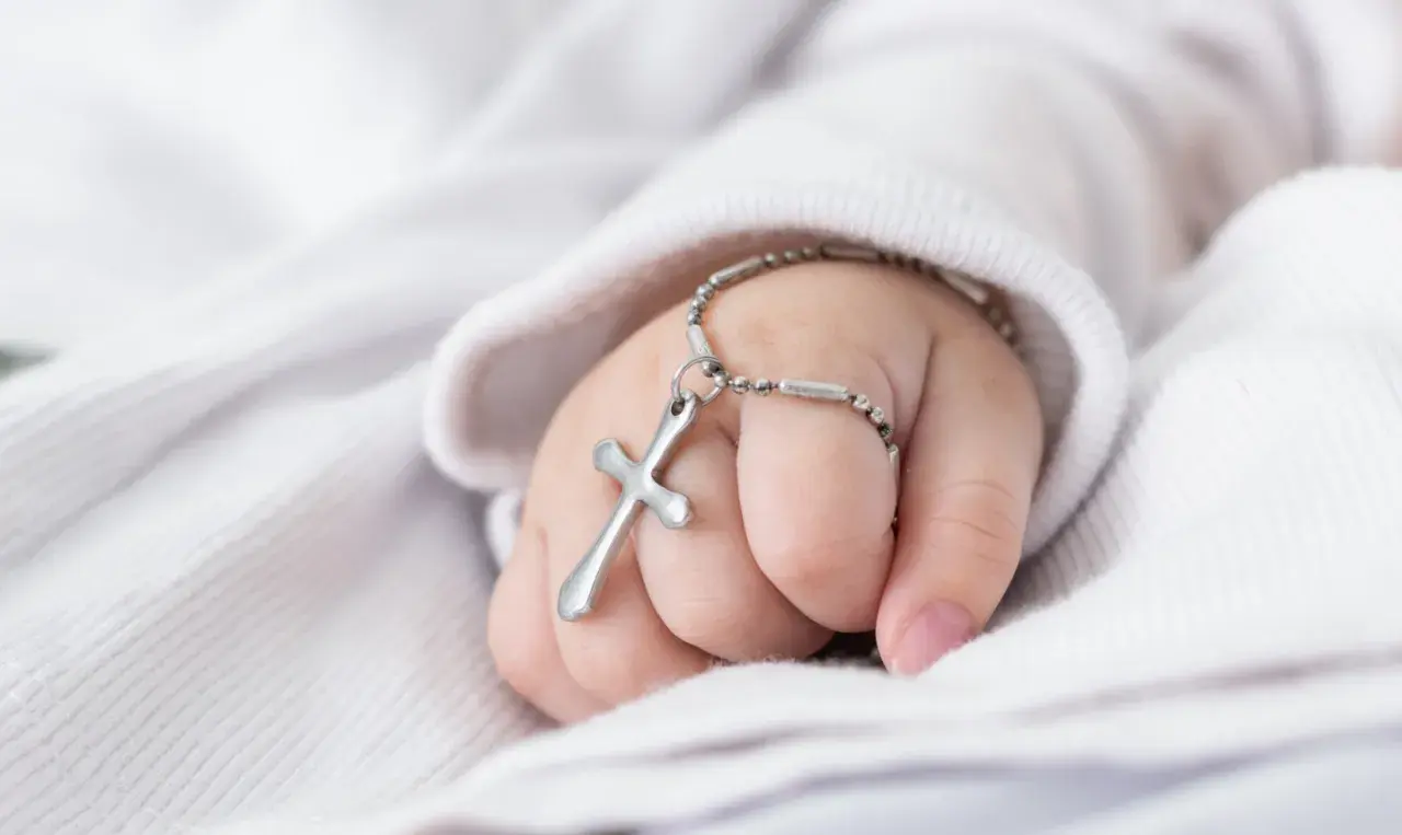 Dziecięca dłoń z krzyżykiem na nadgarstku. Zastanawiasz się, ile trwa msza z chrztem?