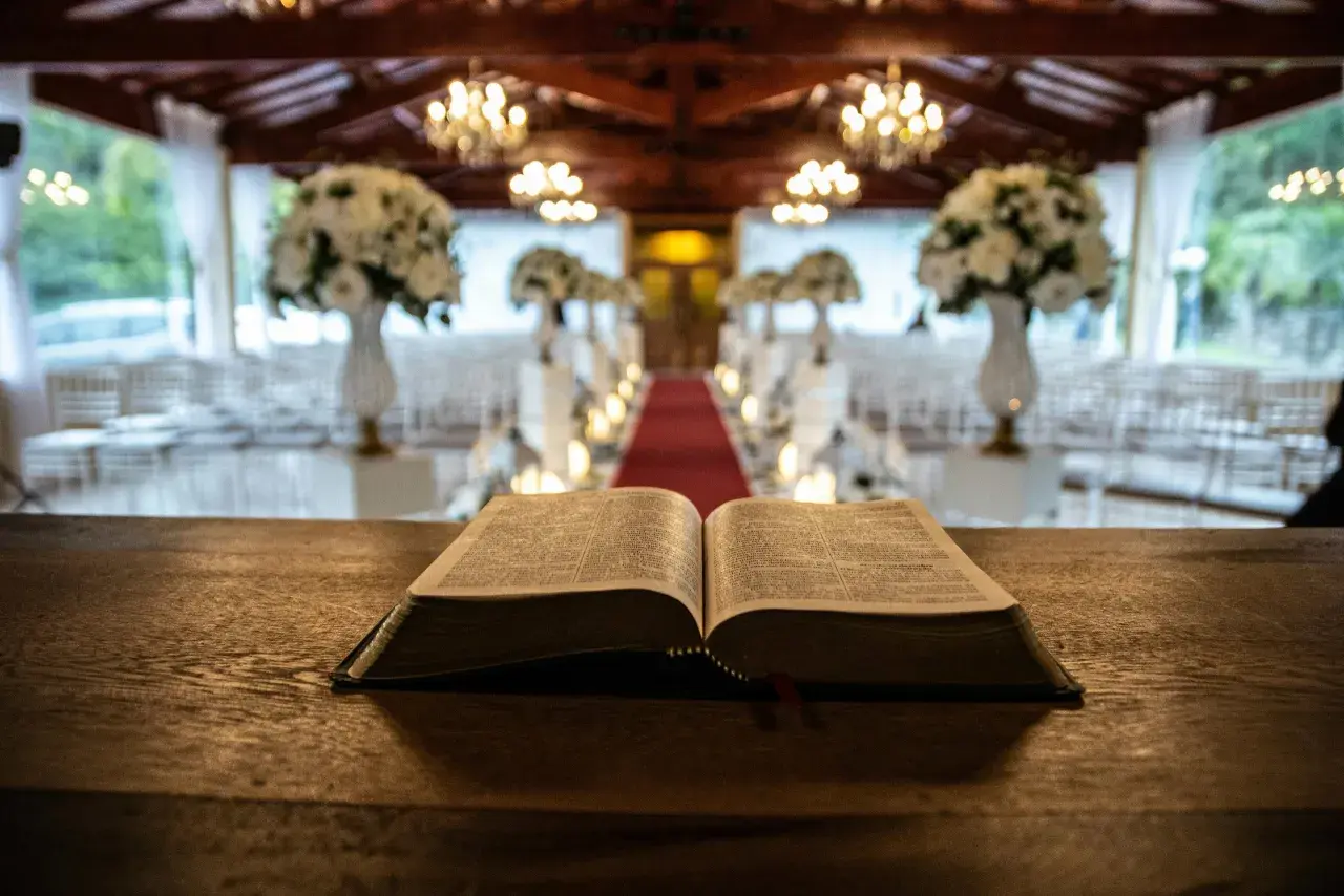Otwarta Biblia na drewnianym stole. W tle udekorowana sala z krzesłami i czerwonym dywanem. Zastanawiasz się, ile trwa msza święta w tygodniu?