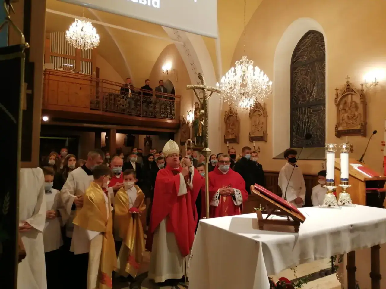 Biskup w czerwonej szacie z krzyżem w ręku, otoczony wiernymi. Czy ksiądz może odmówić bierzmowania? To pytanie nurtuje wielu.