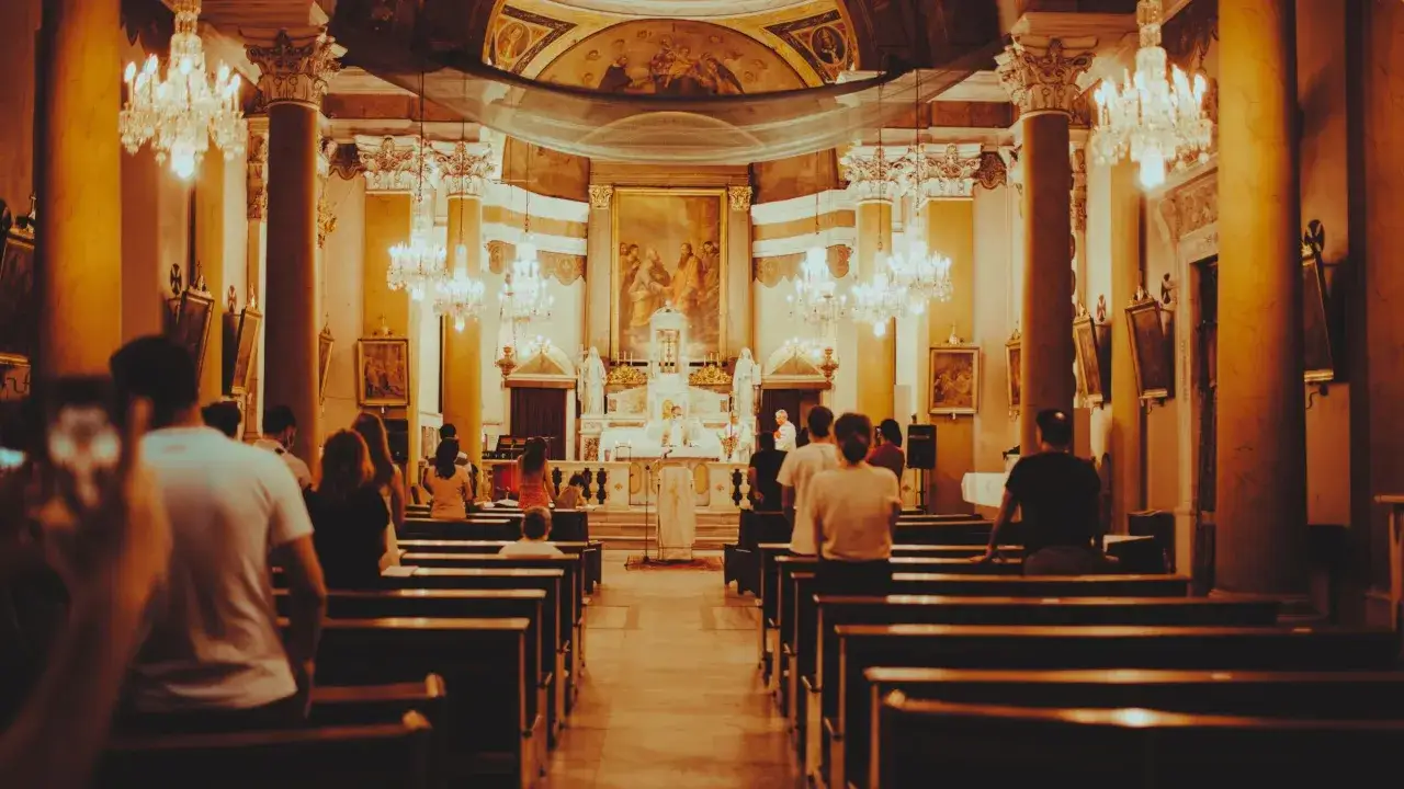 Wnętrze kościoła z wiernymi na ławkach. W oddali ołtarz i celebrans. Wiele osób zastanawia się, ile trwa suma w kościele.