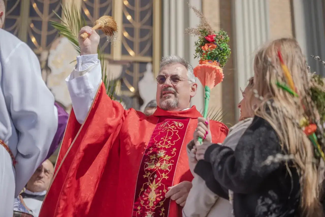 Ksiądz w czerwonej szacie błogosławi wiernych wodą święconą. Zastanawiasz się, ile za mszę w niedzielę?