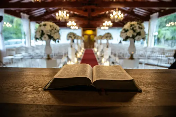 Otwarta Biblia na drewnianym stole. W tle udekorowana sala z krzesłami i czerwonym dywanem. Zastanawiasz się, ile trwa msza święta w tygodniu?